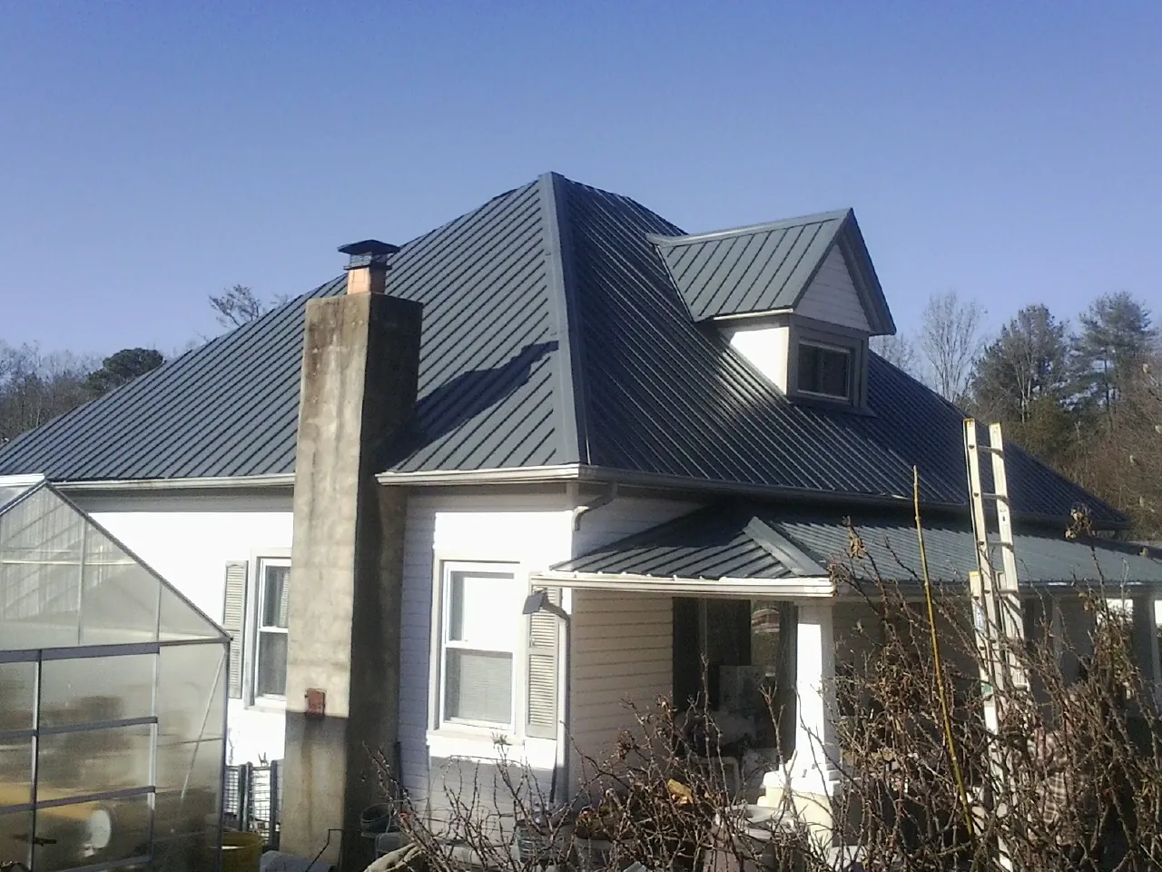 Dark blue standing seam metal roof on a white farmhouse with dormer — Slate & Tile Roof Repair by Roofing Brothers in Foley