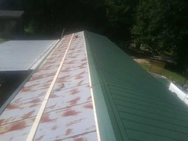 Old rusted panels beside newly installed green metal roofing — Wind Damage Roof Repair by Roofing Brothers in Foley