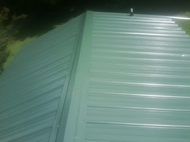 New green metal panels meeting at the ridge of a roof — Flat Roof Repair work by our crew in Foley