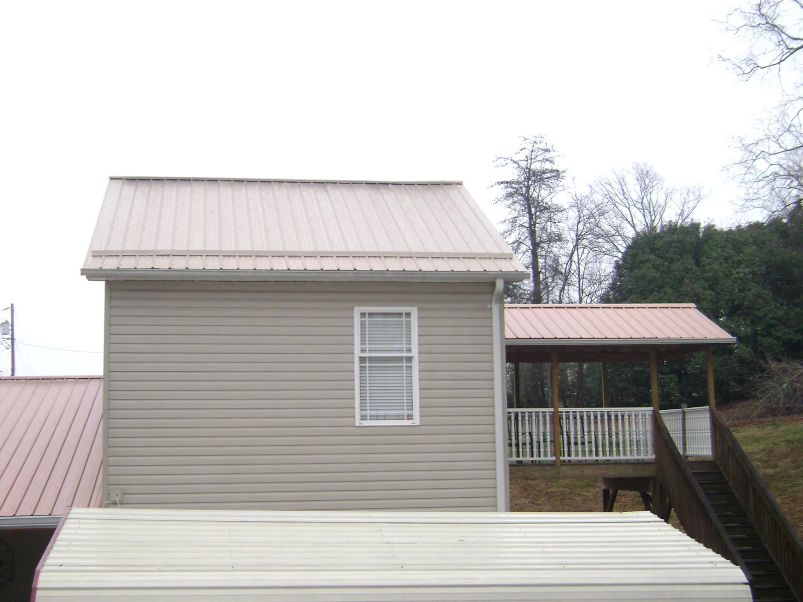 Tan metal roofs on a two story addition and attached porch, from a Roof Replacement job in Foley